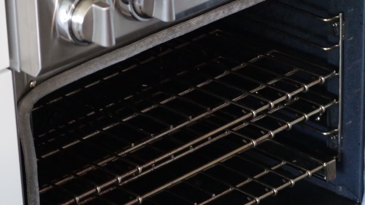 Un guanto da forno apre il forno, estrae una teglia di biscotti natalizi e chiude lo sportello del forno