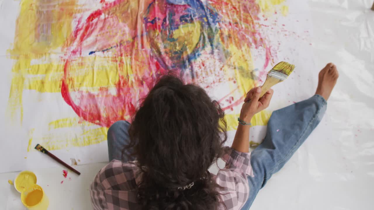 video de una artista femenina biracial pintando en el suelo en un estudio