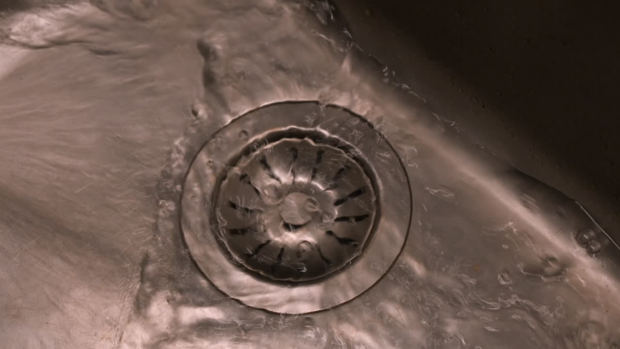 Water from tap flows into stainless steel sink, stopper close up view