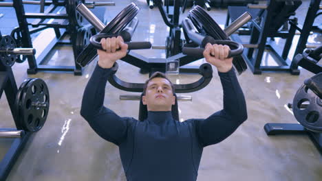 Un-Joven-Musculoso-Entrena-En-El-Gimnasio-Haciendo-Press-De-Banca-En-El-Pecho-En-La-Máquina---ángulo-Alto