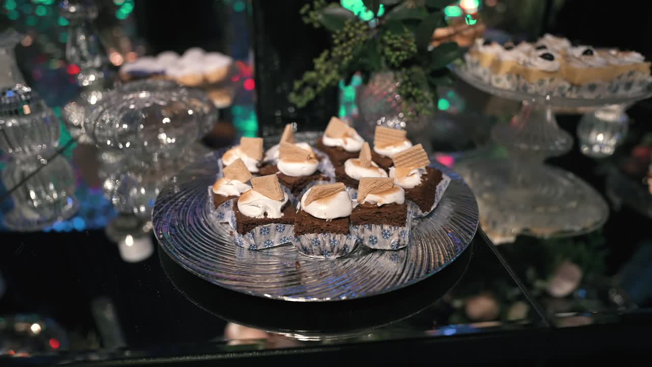 Mini chokoladebrownies med flødeskum og vaffelkager på et sølvfad, en del af et luksuriøst buffetudvalg ved et eksklusivt aftenarrangement, der fejrer succes og nydelse, afsløring i slowmotion