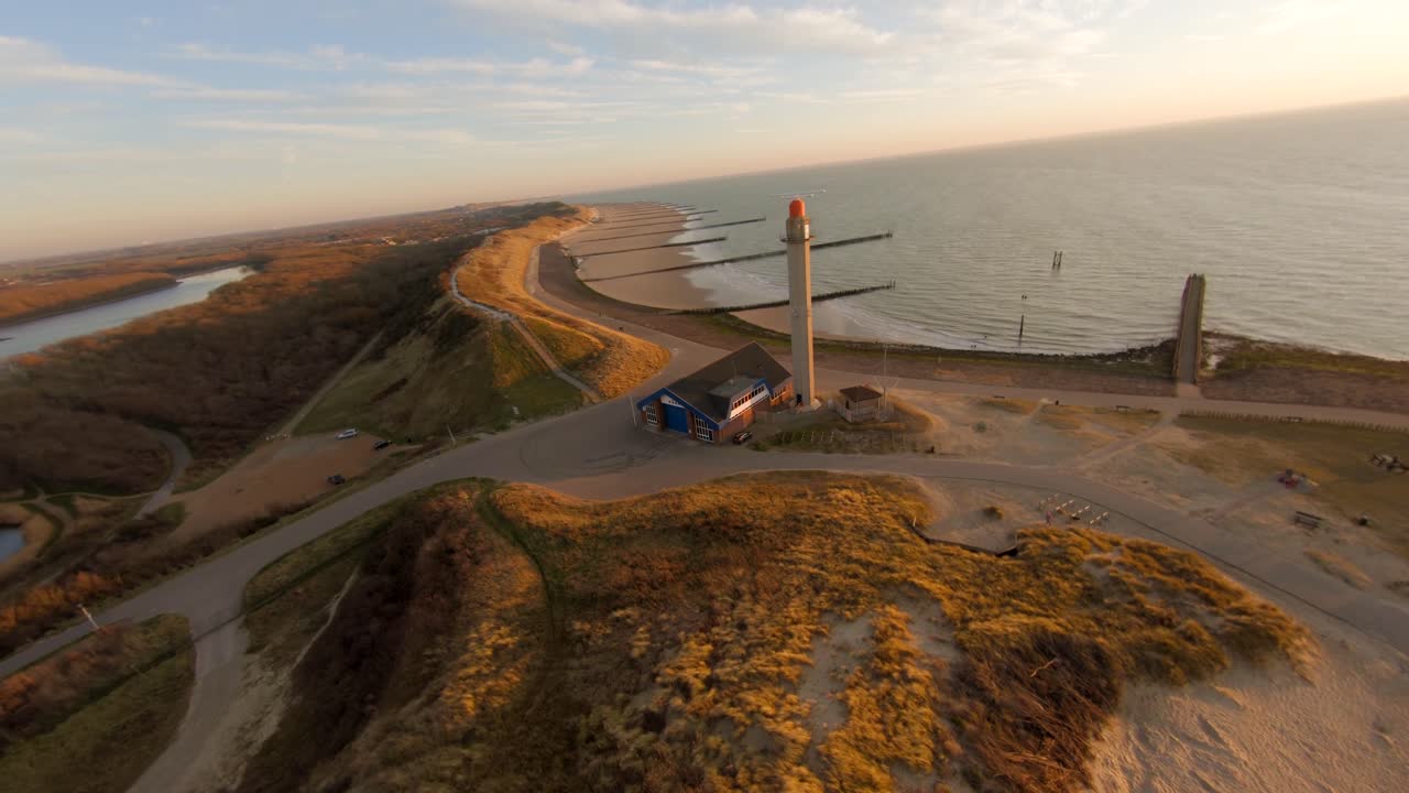 Soaring above the dunes and the beach towards a light house and radar tower in the distance. Aerial shot