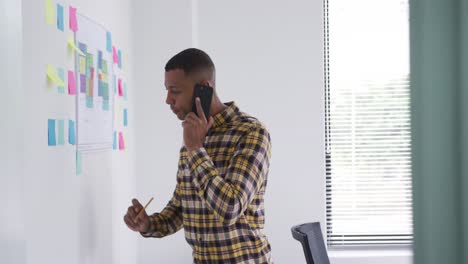 Mixed-race-man-writing-notes-while-on-phone