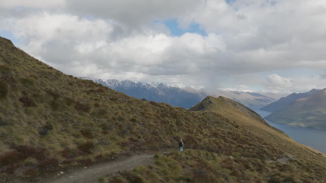mujer rubia caminando por un camino de tierra en los alpes del sur de nueva zelanda, antena