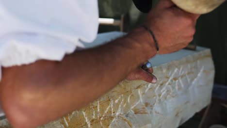 Stone-carver-with-white-shirt-is-hitting-a-stone-with-a-hammer-and-a-chisel-at-a-medieval-market-festival-called-"Wallenstein"-in-Altdorf,-Germany-in-slow-motion