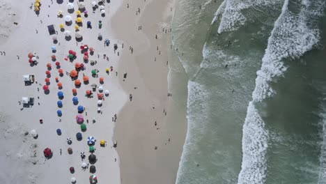 waves rolling into white sand beach full of tourist in cabo frio, rio de janeiro, brazil