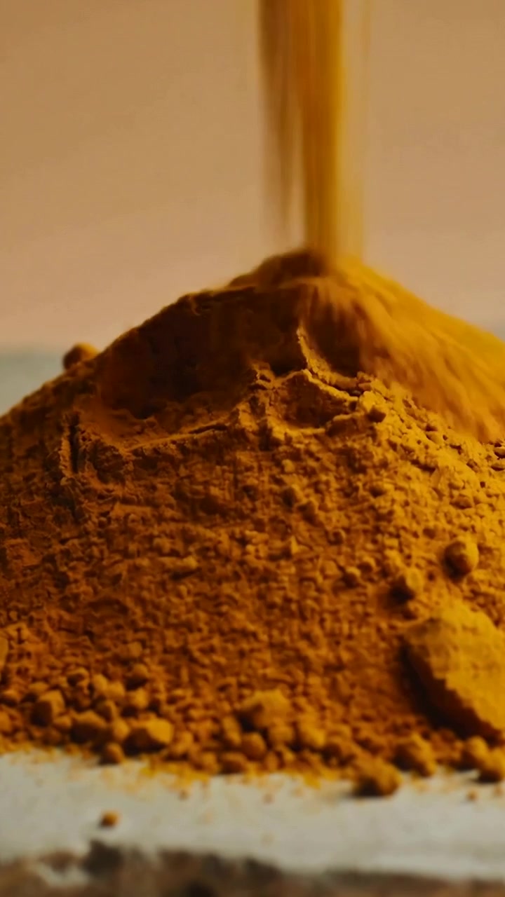 Vertical video: Pouring yellow-orange powder stream building cone on white table, scattering clumps