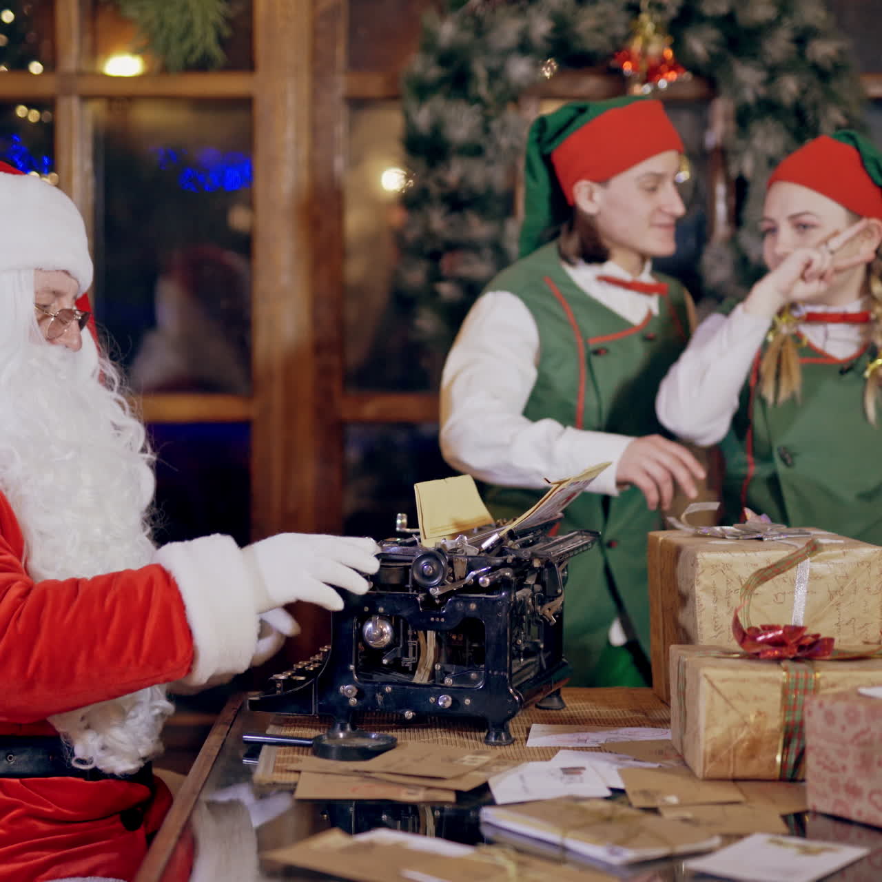 Happy elves in green costumes and Santa in his traditional red suit. Old father Frost berates elves which dance happily in Santa's residence indoors.