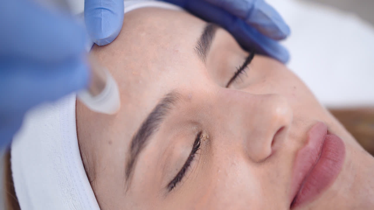 Beautiful slow motion close-up shot of a beautiful young woman's face as she receives a dermatological beauty treatment with a circular massage pen by a female doctor in her clinic.