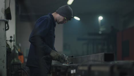 a factory worker works with metal flying sparks in slow motion. a man in protective glasses works with metal grinding polishing and stripping steel metal structures.