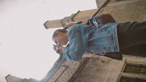 video vertical de una mujer en la calle tomando fotos con una cámara digital de estilo retro para publicar en las redes sociales