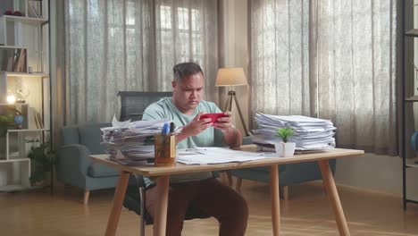 hombre gordo asiático estando molesto perdiendo el juego en el teléfono inteligente después de trabajar con documentos en la oficina