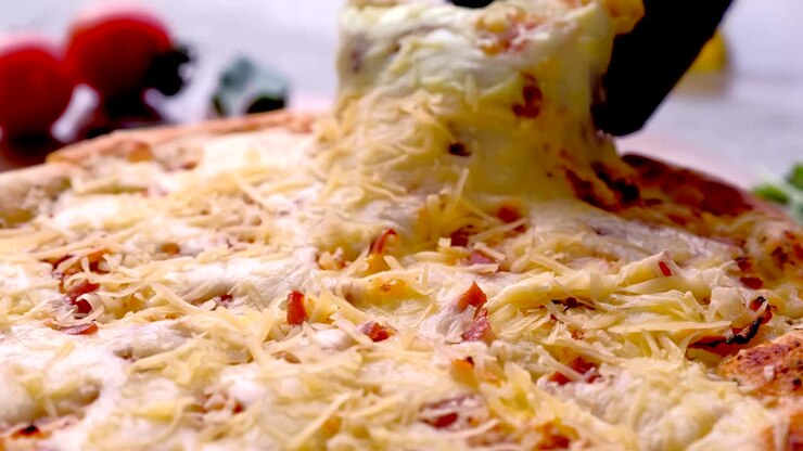 Cuoco prende una fetta di pizza al bacon con formaggio fuso