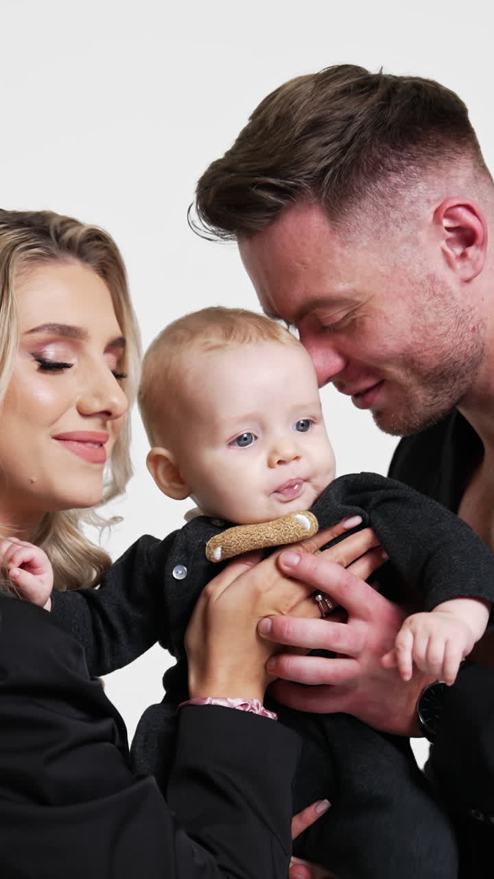 Eltern halten ihr geliebtes kleines Baby von zwei Seiten. Liebende Mama und Papa küssen ihr Kind auf den Kopf. Weißer Hintergrund. Vertikales Video
