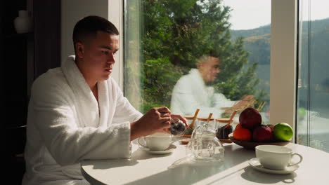 husband brews tea at table in morning. alone man carefully extracts dried tea from container preparing soothing beverage in kitchen. customary morning habit