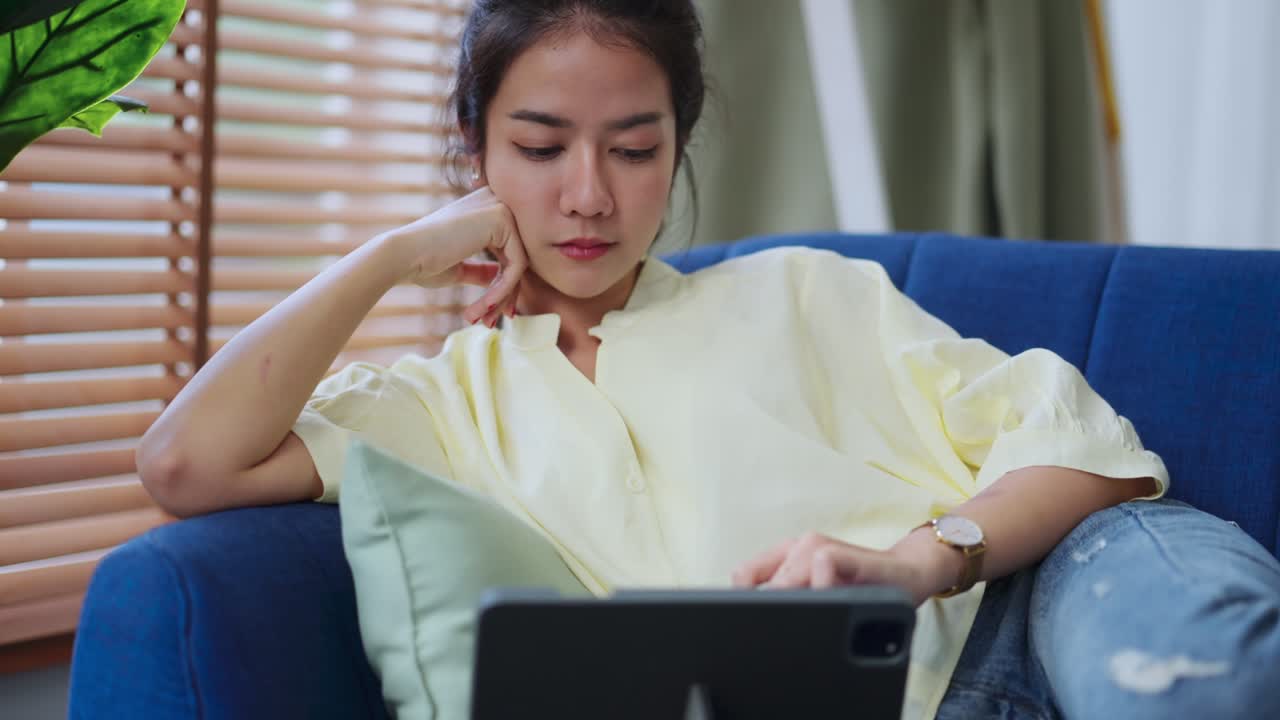 매력적인 아시아 여성 여성은 캐주얼 옷을 입고 집에서 격리됩니다. 거실의 소파에서 태블릿에서 온라인 영화를 즐기십시오.