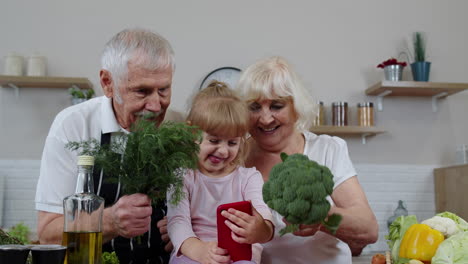 Blogger-grandchild-girl-making-selfie-on-phone-with-senior-grandparents-at-kitchen-with-vegetables