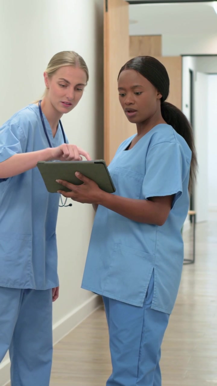 Vertical video: Checking nurses after hi, viewing tablet for chart in hall, stethoscope scrubs