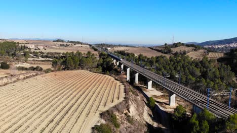 Aerial:-high-speed-train-in-Spain-crossing-a-viaduct-among-vineyards-close-to-Barcelona,-in-Catalonia