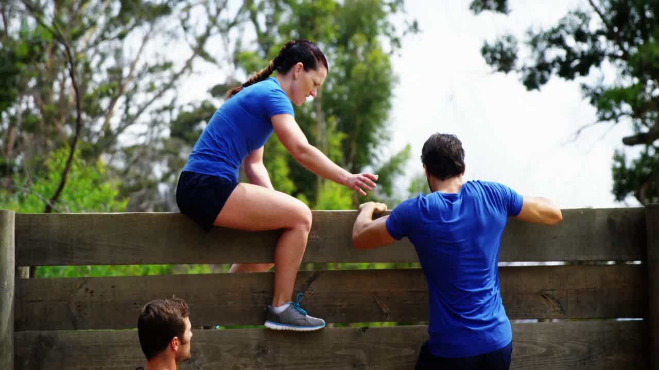 entrenadora ayudando a un hombre en forma a escalar una pared de madera durante una carrera de obstáculos de 4k