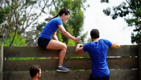 Female-trainer-assisting-fit-man-to-climb-over-wooden-wall-during-obstacle-course-4k