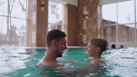 Vater-Und-Sohn-Schwimmen-Und-Planschen-Im-Innenpool-Des-Hotels-Oder-Spa-Centers,-Vergnügen-Sich-Und-Ruhen-Sich-Im-Wellness-Aus