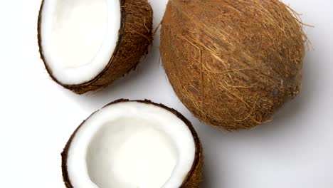 coco tropical maduro y dos mitades de un coco girando sobre un fondo blanco. frutos en bucle