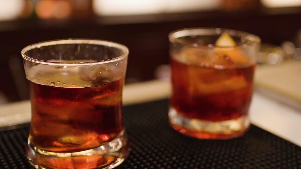 Bartender pours whiskey cocktail over ice in dimly lit bar, warm ambient lighting, close-up
