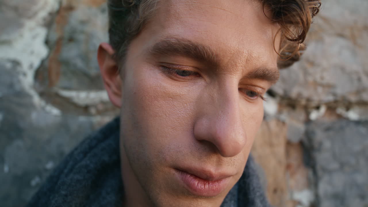 Sad man posing castle wall at windy day portrait. Curly model feeling thoughtful