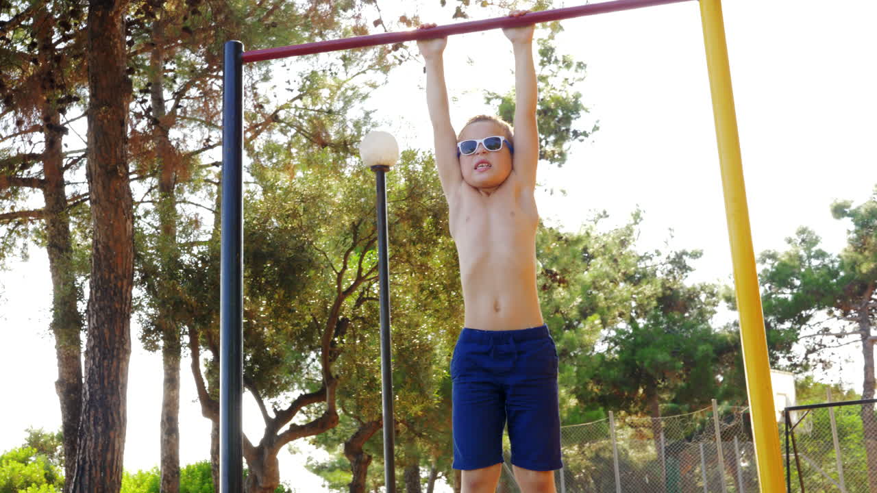 niño haciendo ejercicio en una barra de chin-up en un campo deportivo al aire libre