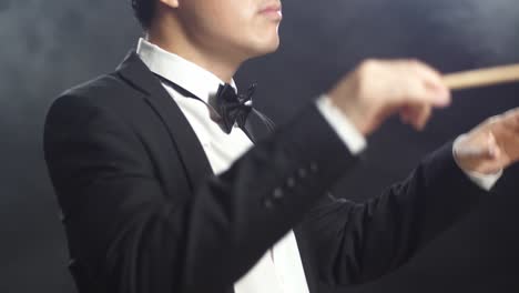 안개가 가득한 검은 스튜디오에서 눈을 감고 몸짓을 보이는 아시아계 지휘자 남자.