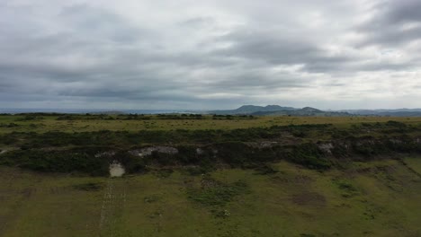 Ascending-flight-with-a-drone-over-a-level-mountain-with-a-surprise-effect,-a-discovery-was-made-of-the-sea-and-the-mouth-of-a-river-on-a-cloudy-morning-in-summer-in-Cantabria-Spain