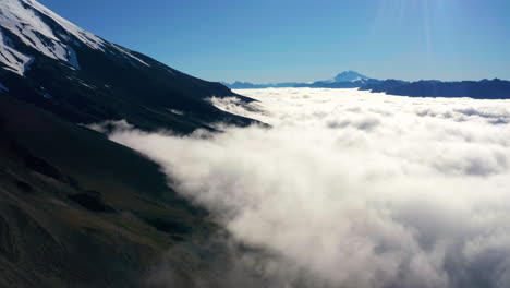 aerial shot above low lying clouds in chilean national park vicente perez rosales showing snow peaked mountains