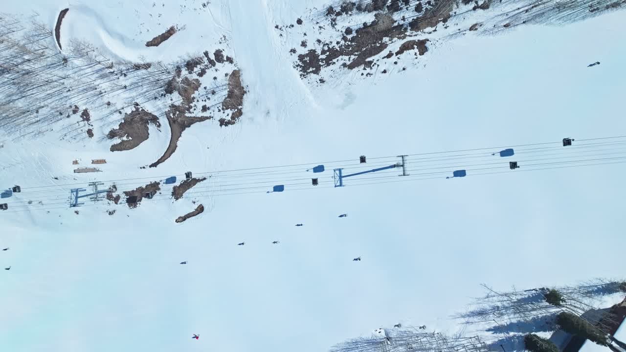 Winter landscape with skiers descending wide slope framed by snow-laden condos and rocks weaving through ski lift shadows, Snowmass Colorado USA