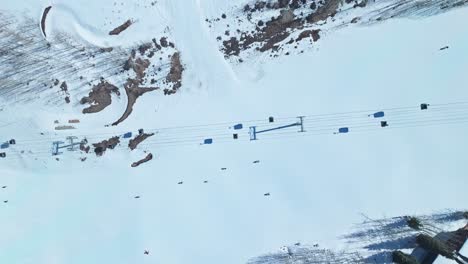 winter landscape with skiers descending wide slope framed by snow-laden condos and rocks weaving through ski lift shadows, snowmass colorado usa