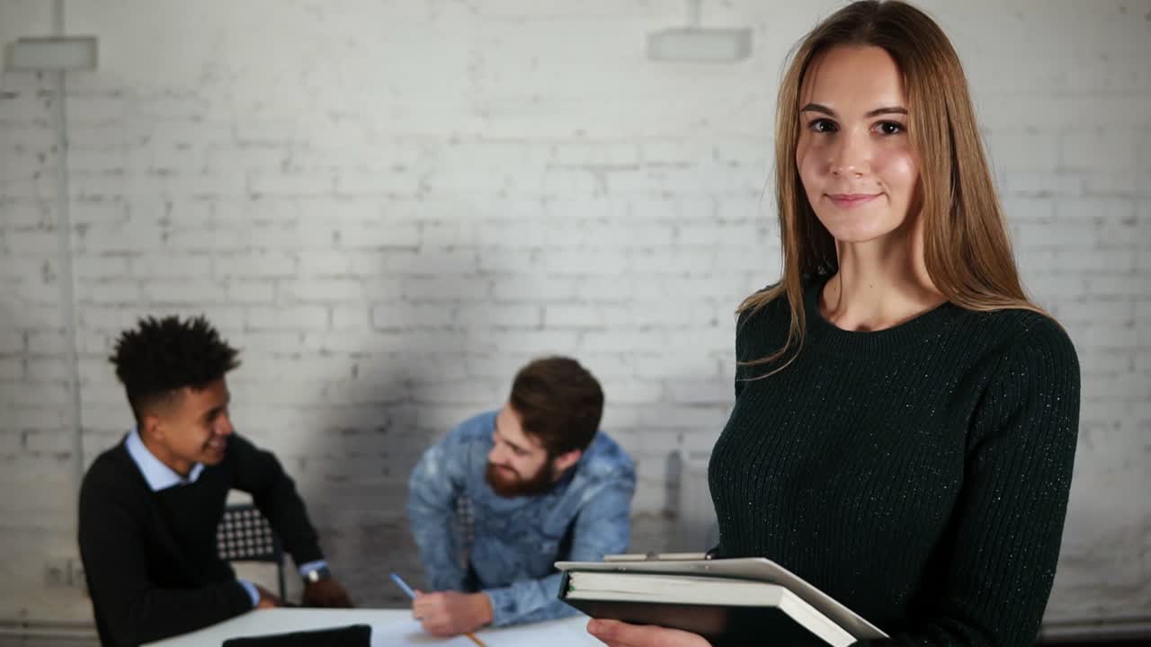 retrato de una feliz mujer de negocios en la oficina con sus colegas sosteniendo una carpeta con documentos y mirando a la cámara.