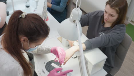 overhead view of nail technician wearing pink gloves filing client fingernails using hand file at modern manicure station, showcasing detailed nail care service in bright, well-lit salon environment
