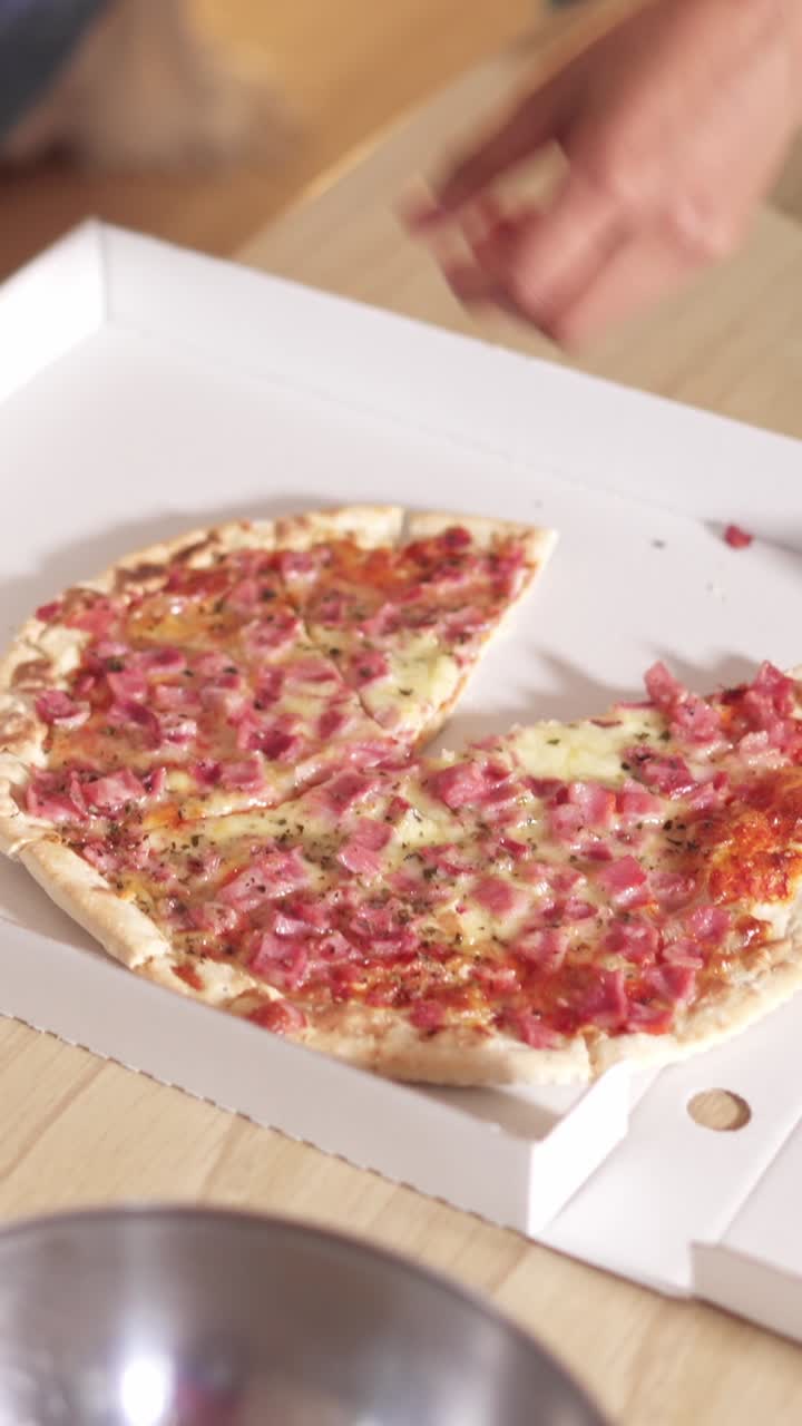 Half-eaten pizza with ham and cheese in a delivery box