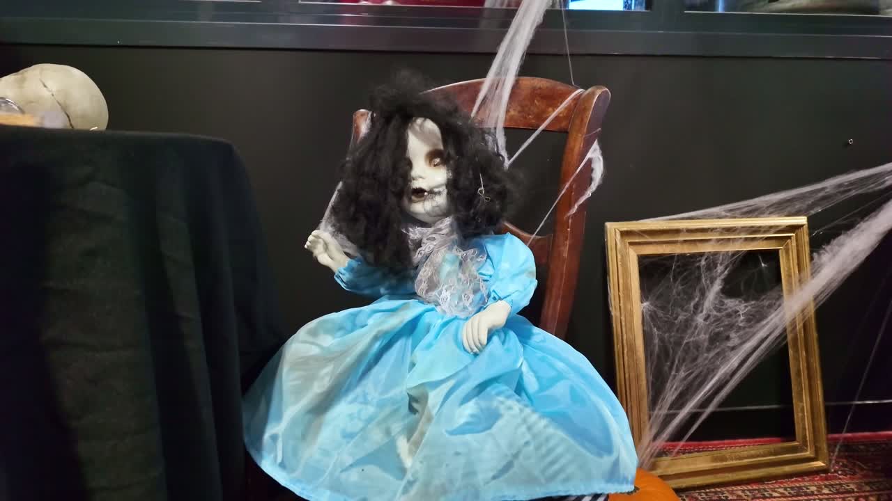 Creepy haunted doll in blue dress sitting on dark table as Halloween decoration
