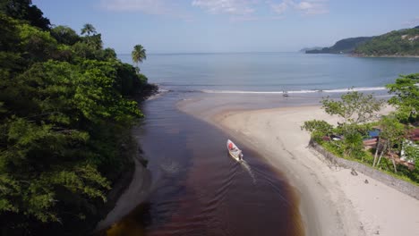 Vista-Aérea-Siguiendo-Un-Barco-Que-Sale-De-Un-Río-Hacia-El-Océano-En-Barra-Do-Sahy,-Brasil