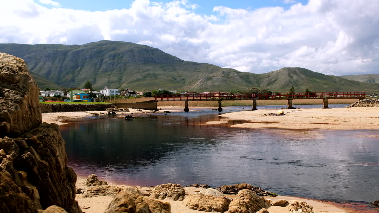 Slider from behind rock on beach reveals foot bridge and Kleinmond lagoon