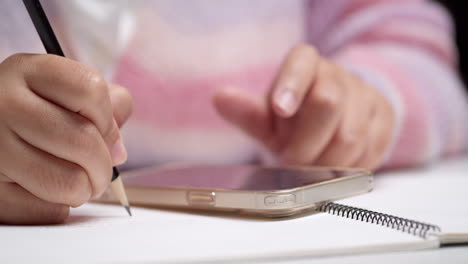 woman writes down personal income and expenses from her phone into a notebook for financial analysis