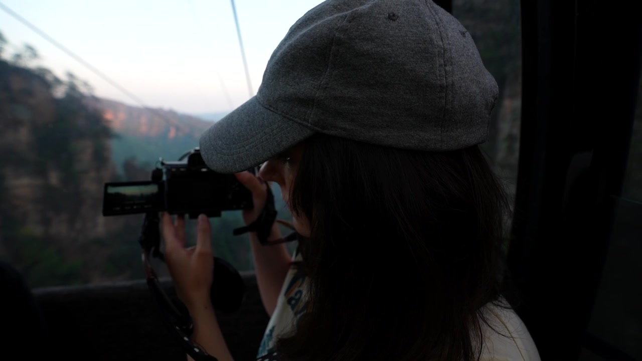 Young woman tourist with a baseball cap filming a beautiful mountain landscape from a cable car