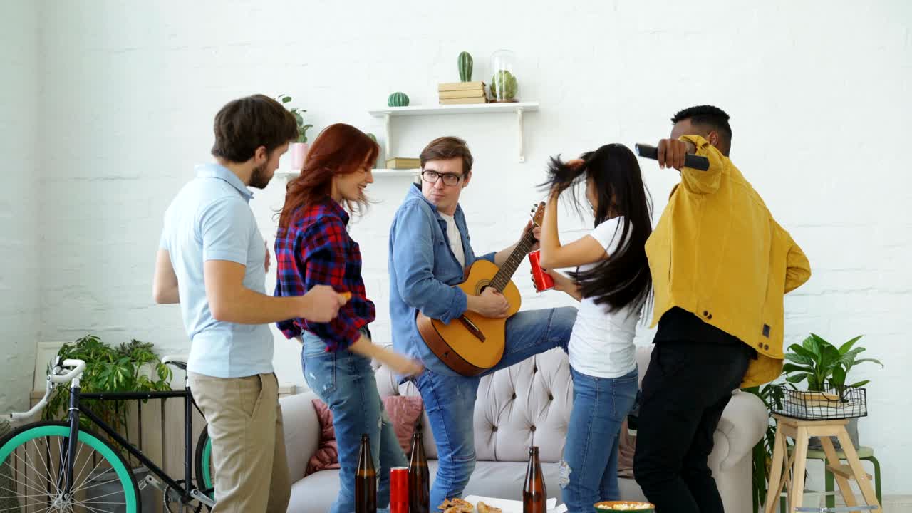 다민족 친구 그룹이 집 파티를 하면서 춤추고 기타를 연주하고 있습니다.