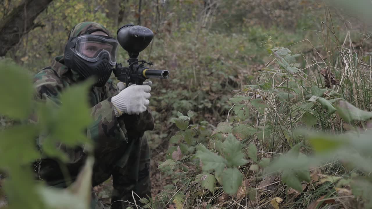 Paintball player in grass shoots in slow motion