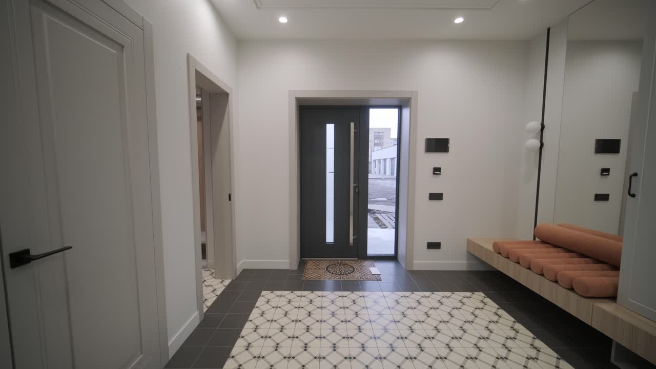 The entryway of a modern home with patterned floor tiles, elegant white doors, and a wooden bench with orange cushions, creating a welcoming and stylish atmosphere