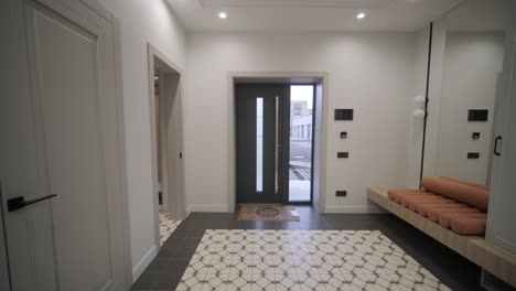 la entrada de una casa moderna con azulejos de piso con patrones, puertas blancas elegantes y un banco de madera con cojines naranjas, creando una atmósfera acogedora y elegante