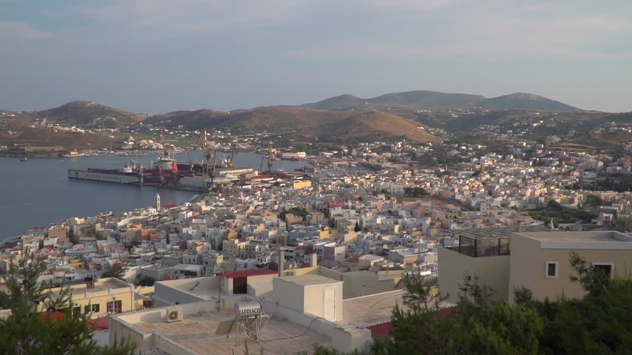 barrido panorámico derecho en movimiento lento sobre la ciudad de syros al atardecer desde lo alto con colinas y montañas en la distancia