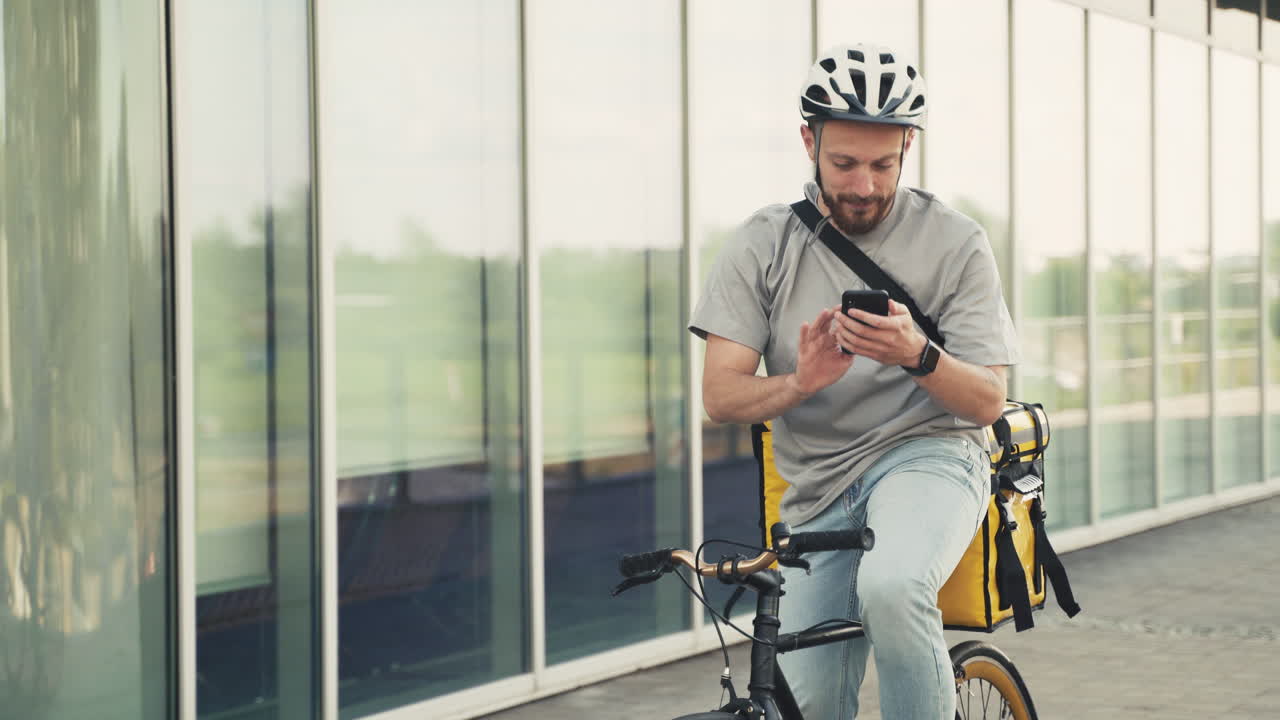 repartidor de comida feliz con mochila térmica en su bicicleta echando un vistazo a su teléfono inteligente