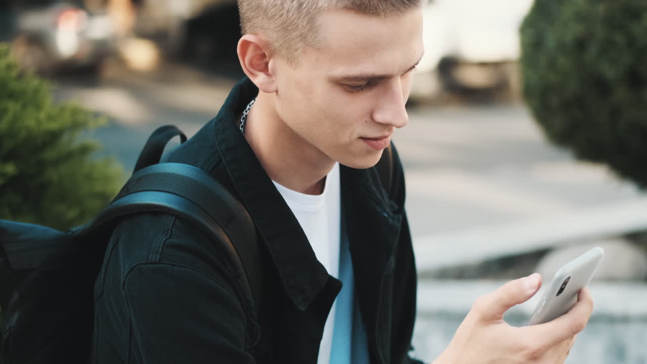 молодой студент использует мобильный телефон на открытом воздухе.